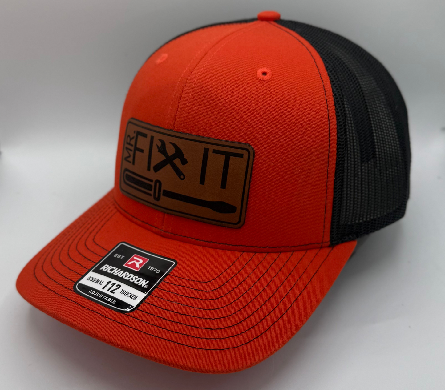 Orange and black trucker hat with a structured front panel and black mesh back, featuring a curved brim and contrasting black stitching on the visor and crown.