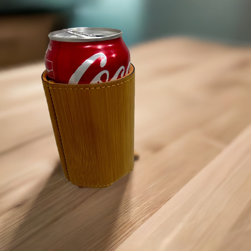 A custom bamboo leatherette Koozie holding a red Coca-Cola can, placed on a light wooden surface. The Koozie features a smooth, wood-grain textured finish with neat stitching along the top edge, offering a rustic and eco-friendly aesthetic. Ideal for personalized gifts or promotional items.