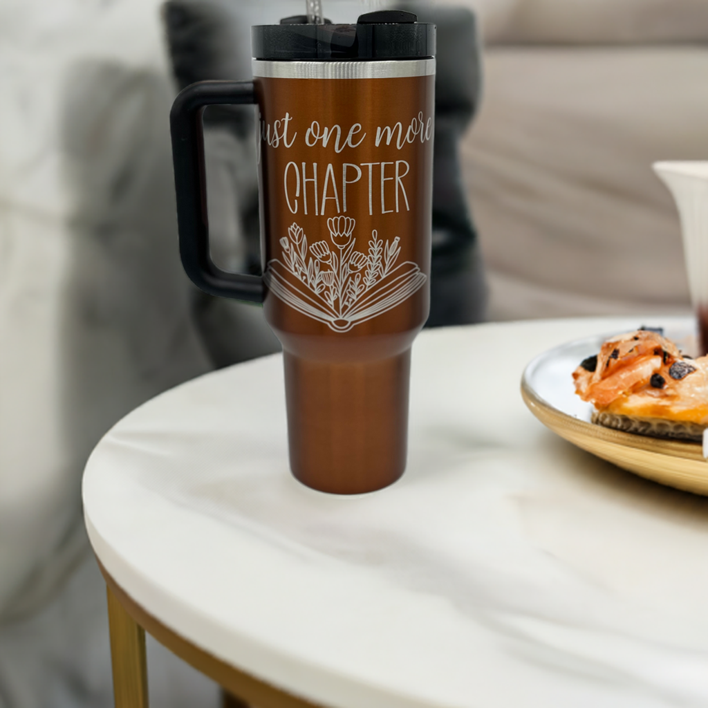 "Custom personalized copper 40oz Stanley tumbler with an engraved 'Just One More Chapter' design, featuring an open book with floral details. Includes a sturdy black handle and lid, perfect for book lovers and coffee enthusiasts alike."