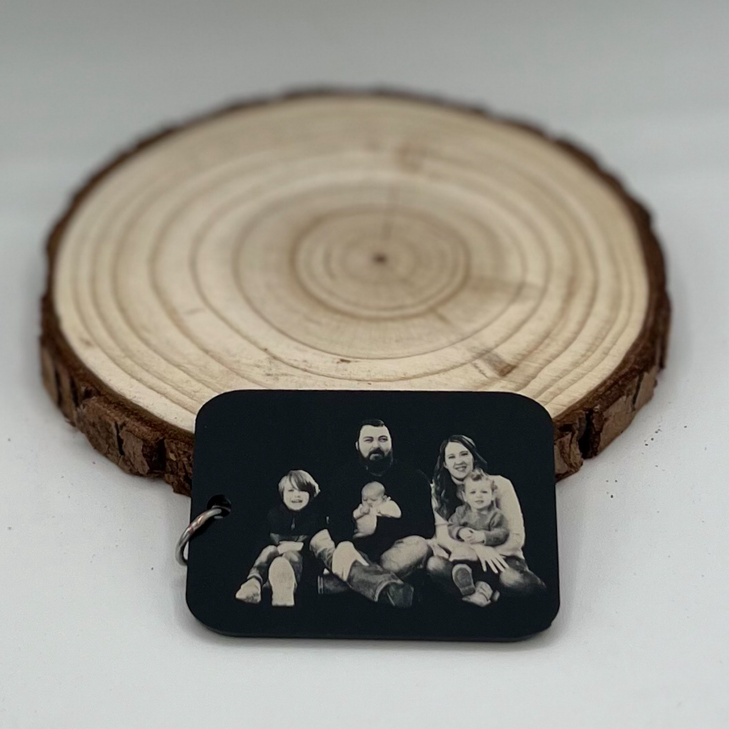 "Custom matte black acrylic keychain or necklace featuring an engraved family photo, displayed on a rustic wooden background."