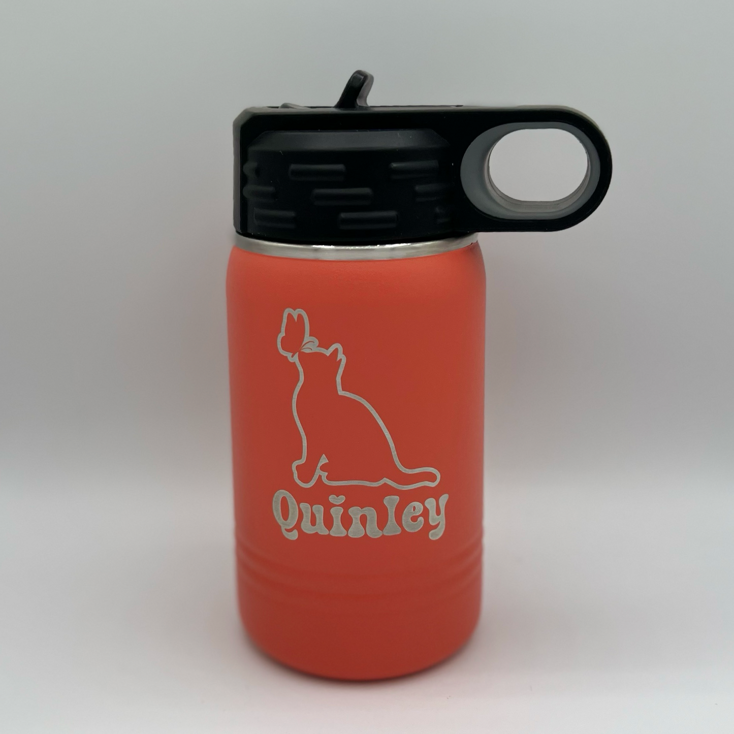"Custom personalized coral Polar Camel 12oz stainless steel kids' water bottle with a black flip-top lid and handle. The bottle features an engraved design of a cat gazing at a butterfly, along with the name 'Quinley' in a playful, bold font."