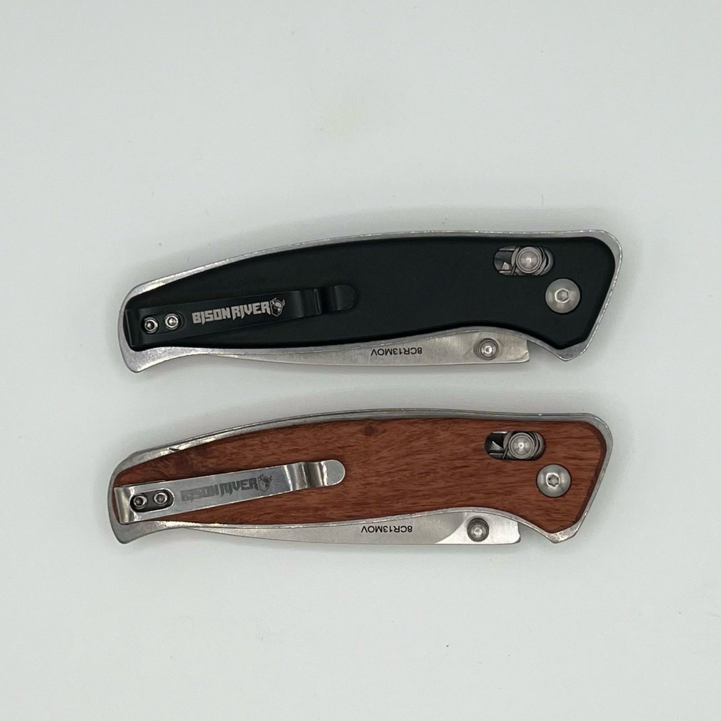 Back side view of personalized engraved Bison River pocket knives featuring black and wood handles. The metal clips are engraved with the Bison River logo, showcasing a practical and stylish design perfect for everyday carry.