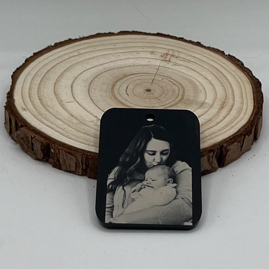 "Matte black acrylic photo keychain or necklace featuring a laser-engraved image of a mother lovingly holding her baby, displayed on a rustic wooden background."