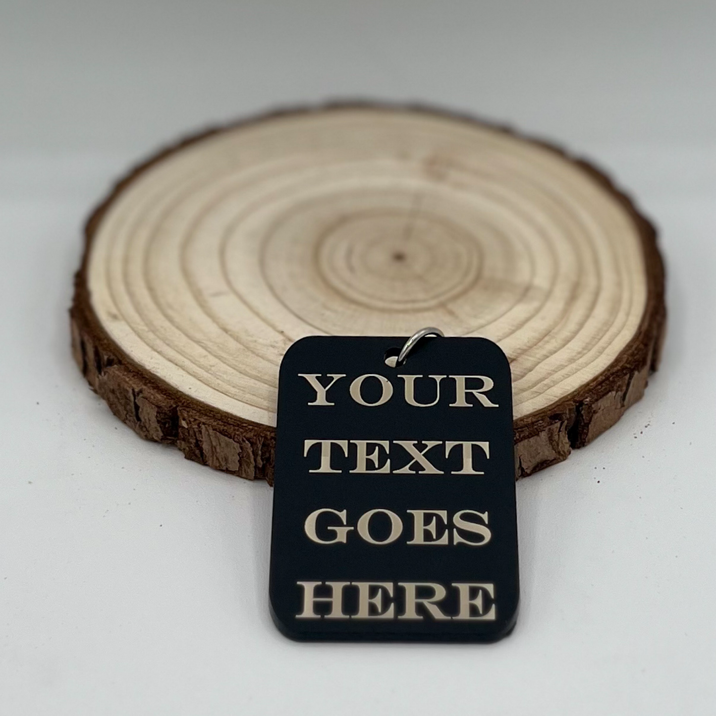 "Custom matte black acrylic keychain or necklace with engraved text placeholder 'YOUR TEXT GOES HERE,' displayed on a rustic wooden background."
