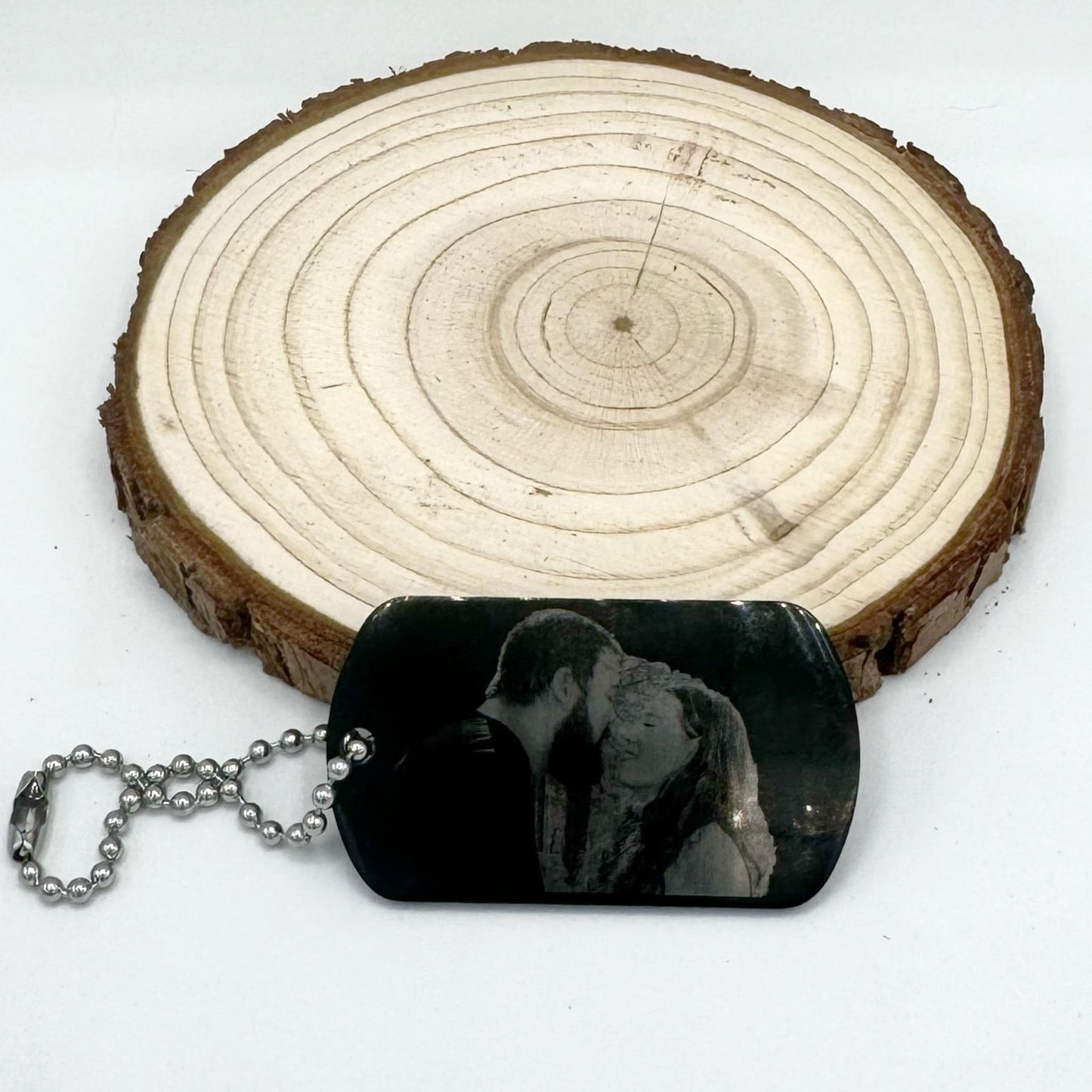 "Custom black stainless steel dog tag keychain or necklace featuring an engraved photo of a couple sharing a loving moment, with a rustic wooden background.