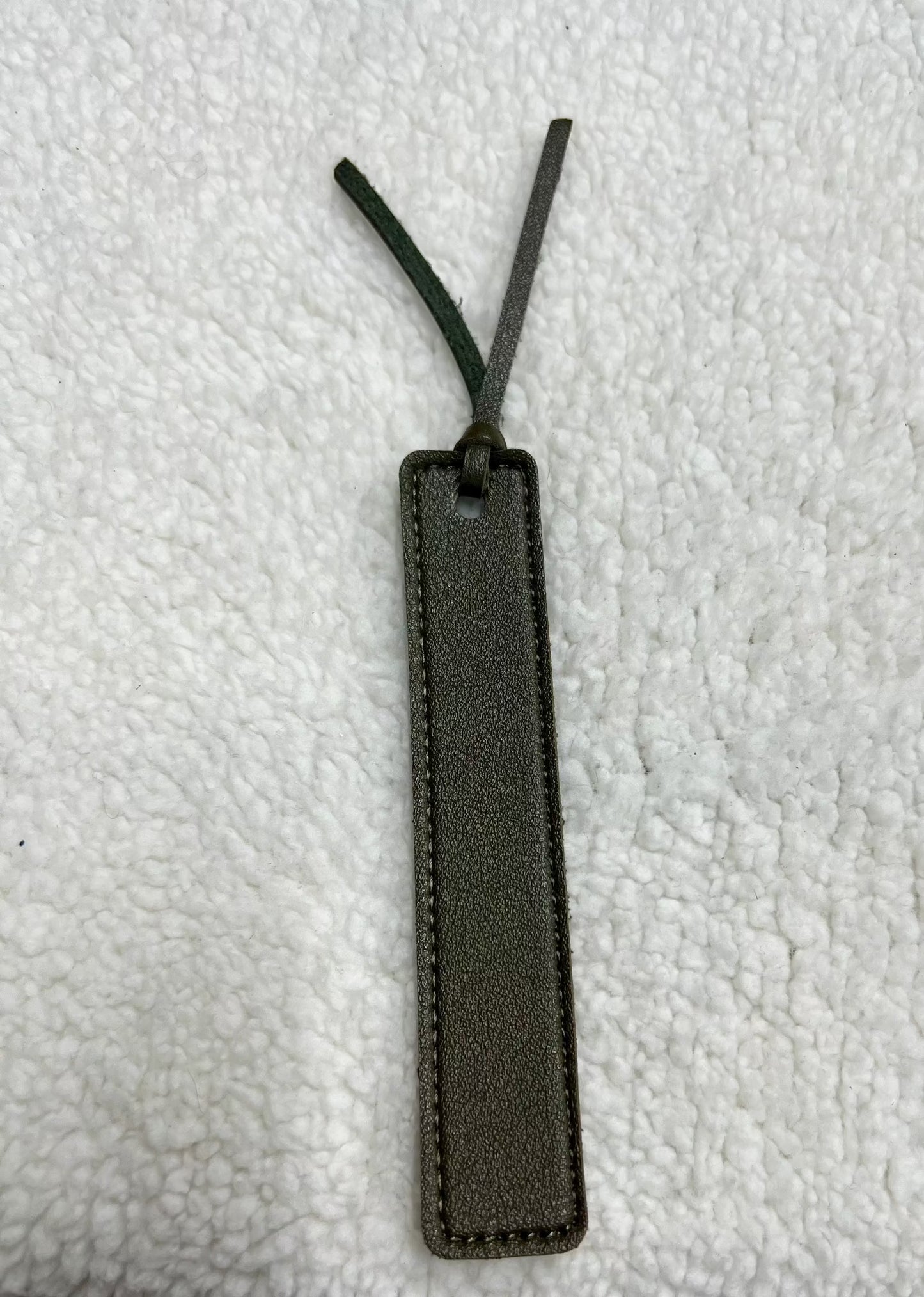 A MOON AND SKYE CREATIONS LLC leather bookmark in dark green, featuring a tassel and laser engraving, lies elegantly on a textured white surface.