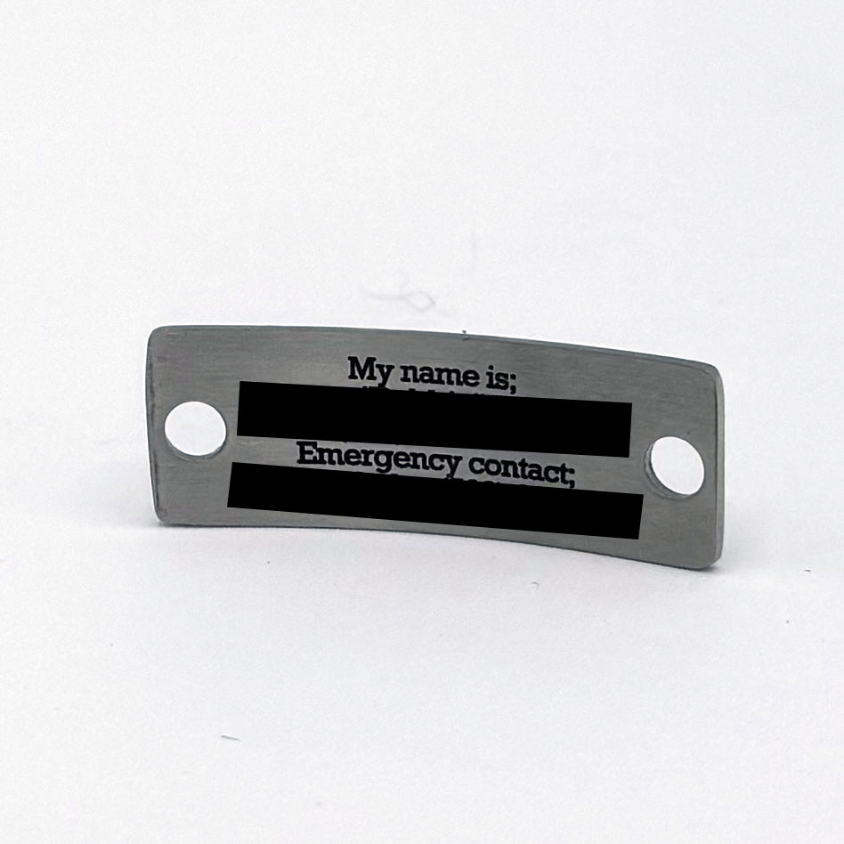 Back view of a stainless steel medical alert pendant with a brushed finish. The surface is smooth and metallic, featuring two holes for attachment, with blank space for engraving personal details. The tag is curved slightly for a comfortable fit.