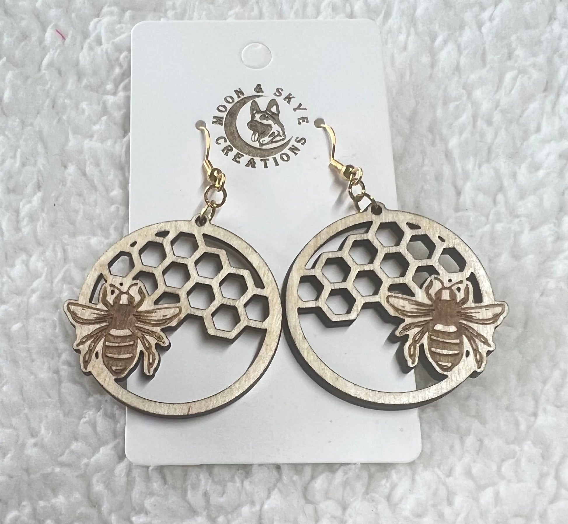 Wooden earrings featuring a circular honeycomb design with a detailed bee accent layered on top. Crafted by Moon & Skye Creations, these lightweight earrings offer a charming, nature-inspired aesthetic with intricate laser-cut detailing and a natural wood finish.