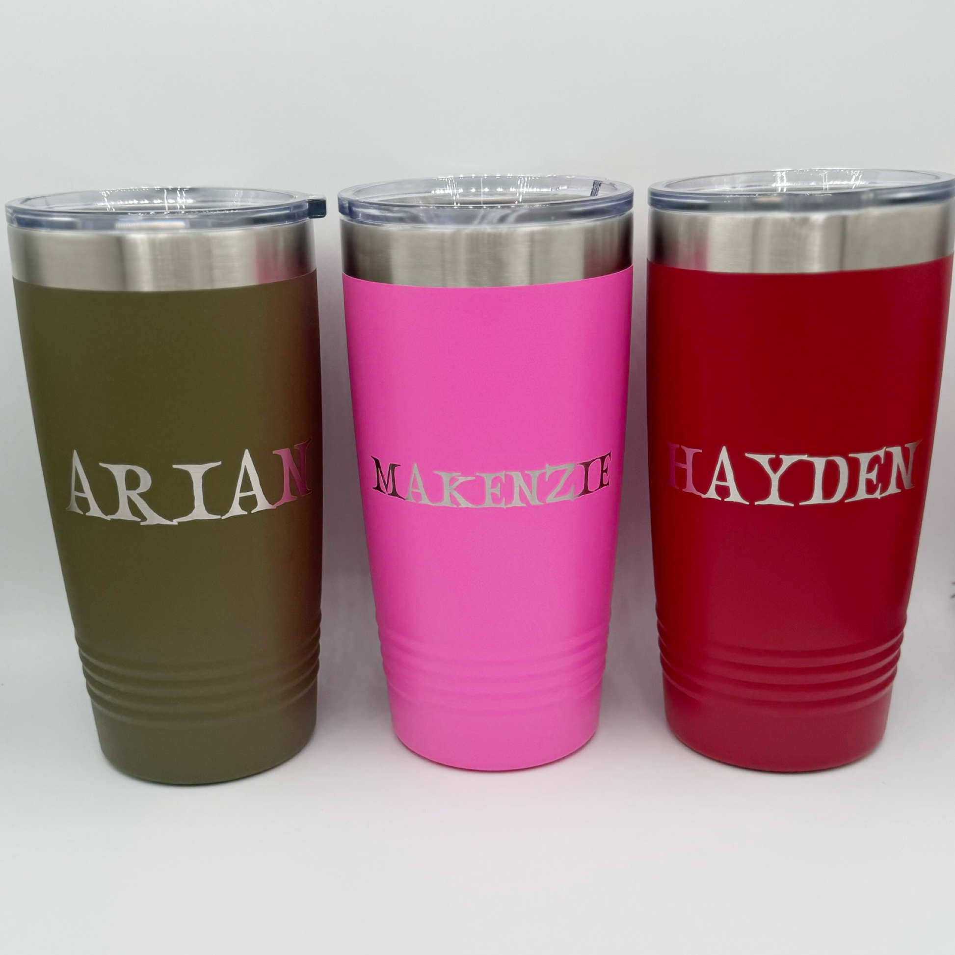 "Personalized 20 oz Polar Camel tumblers with engraved names ARIAN, MAKENZIE, and HAYDEN in stainless steel finish on matte olive, pink, and red insulated cups."