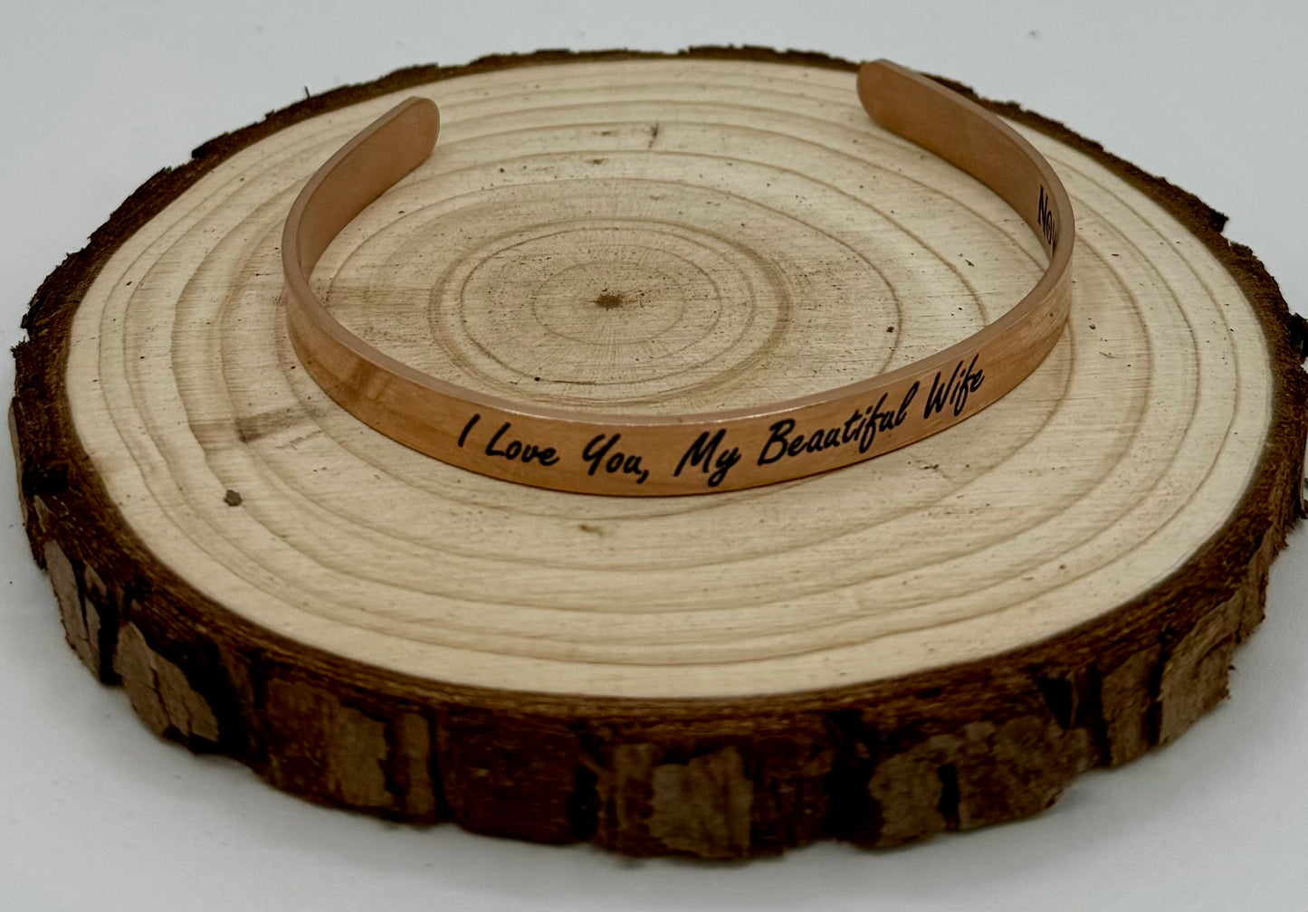 "Moon and Skye Creations personalized rose gold cuff bracelet with an engraved message, 'I Love You, My Beautiful Wife.' A sentimental and elegant gift, displayed on a rustic wooden slice."