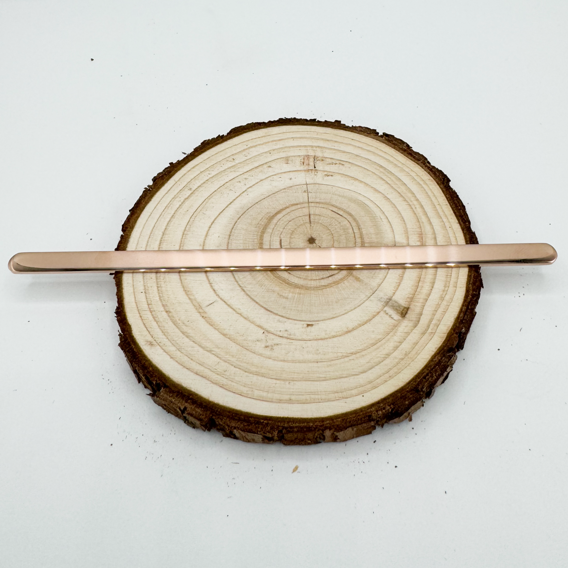 "Moon and Skye Creations personalized rose gold cuff bracelet in a flat, unshaped form, displayed on a rustic wooden slice. A sleek and minimalistic jewelry piece, ready for customization and shaping."
